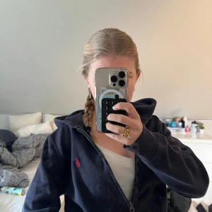 Mörkblå hoodie från Polo Ralph Lauren - Snygg mörkblå hoodie från Polo Ralph Lauren med dragkedja och huva. Klassisk röd logga broderad på bröstet och mjukt material som känns skönt mot huden. Perfekt för en avslappnad och stilren look. Kontakta om ni har frågor