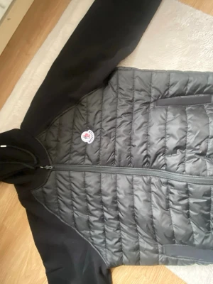 Svart pufferjacka från Moncler - Snygg svart pufferjacka från Moncler med quiltad front och mjuka ärmar i sweatshirtmaterial. Jackan har huva, dragkedja framtill och två fickor. Moncler-logga på bröstet ger en exklusiv vibe. Perfekt för dig som vill ha både stil och komfort. det är en 1.1kopia. XXL känns som XL. passar båda könen. 