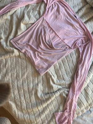 Ljusrosa omlottopp med långa ärmar - Säljer en ljusrosa omlottopp med långa ärmar. Toppen har en snygg omlottdesign framtill och är gjord i ett mjukt, tunt material som känns skönt mot huden. Perfekt att styla med jeans eller kjol för en trendig look.