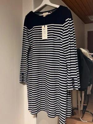 Marinblå och vit randig klänning - En klassisk marinblå och vit randig klänning från Lindex. Klänningen har lång ärm, rund halsringning och dekorativa knappar på axlar och ärmslut. Slutsåld överallt!