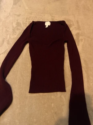 Mörkröd ribbad långärmad topp - Trendig mörkröd långärmad topp med ribbad struktur och figurnära passform. Toppen har en snygg sweetheart-ringning och är tillverkad i stretchigt material som sitter tight. Perfekt att styla med jeans eller kjol för en cool look.