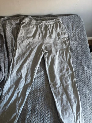 Gråa och svarta mjukisbyxor från Nike - Få båda två för 250! Snygga gråa och svarta mjukisbyxor från Nike med dragsko i midjan och resår. Byxorna har sidofickor och en broderad Nike-logga på vänster ben. Tillverkade i mjukt bomullsmaterial för maximal komfort.