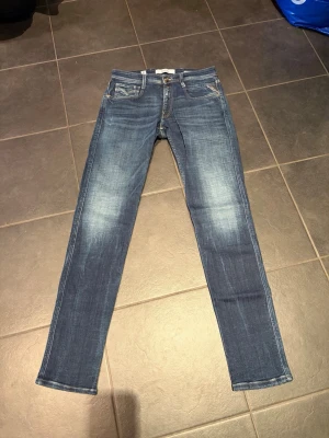 Blå replay jeans  - Ett par blå slimfit jeans med snygga slitningar och ljusare partier på låren och knäna. Läderpatch bak i midjan. Tillverkade i denim med stretch. Använd endast ett fåtal gånger, inga tecken på slitningar vid fotsömmarna