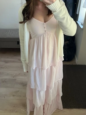 Ljusrosa långklänning med volanger - Ljusrosa långklänning med volangdetaljer och v-ringning från Kappahl i storlek xs. Klänningen har tunna axelband och knappar framtill. Klänningen är i nyskick! ☀️nypris va 799kr o skulle säga att den passar xs/s. 