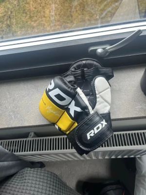 RDX MMA-handskar S - Säljer ett par MMA-handskar från RDX i svart, gul och vit färg. Handskarna har öppen tumme och kardborreband för bra passform. Väldigt bekväma vid grappling och MMA. Knappt använda, typ en två gånger. Storlek S
