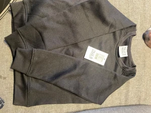 Svart sweatshirt från Tilly & Maddox - En enkel och stilren svart sweatshirt från Tilly & Maddox. Tröjan har rund halsringning, ribbade muddar vid ärmslut och nederkant samt en mjuk bomullskänsla. Perfekt för en avslappnad look och lätt att matcha med andra plagg.