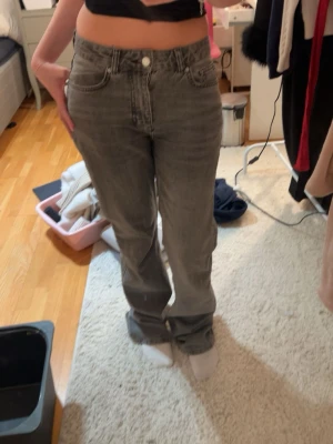 Grå raka jeans från Gina Tricot - Säljer ett par grå jeans från Gina Tricot med rak passform och klassisk femficksdesign. Jeansen har hög midja, knapp- och dragkedjestängning samt stora bakfickor. Materialet är denim i bomull och färgen är tvättad grå.