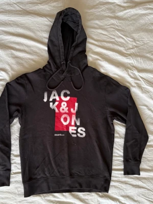 Jack & Jones hoodie - Säljer min svarta Jack & Jones hoodie i storlek M. Snyggt vitt och rött tryck framtill. Obs! Det finns ett litet hål precis under trycket (se bild), men den har absolut mer att ge och är perfekt som en skön vardagshuvtröja. Det finns även noppor på insidan! Materialet är mjuk bomullsmix. 