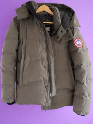 Canada Goose Jacka - Säljer en exklusiv dunjacka från Canada Goose i en stilren mörkgrå färg. Jackan är i mycket fint skick och perfekt för kalla vinterdagar. Den är både varm, bekväm och vind-/vattenavvisande – perfekt för svenska vintrar.  ✔ Klassisk modell med ikonisk logga på armen ✔ Hög kvalitet med riktigt bra isolering ✔ Flera praktiska fickor ✔ Tidlös design som passar allt  Storlek: S Skick: Mycket bra