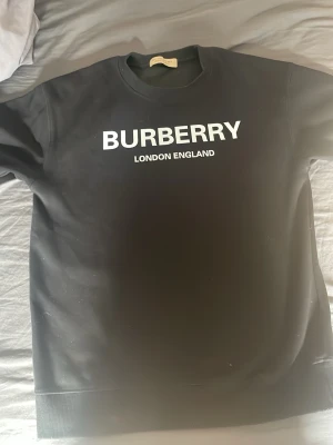 Svart Burberry tröja  med tryck - Snygg svart hoodie från Burberry med vit text 'BURBERRY LONDON ENGLAND' på bröstet. Har används fåtal gånger. Storlek M men passar även S