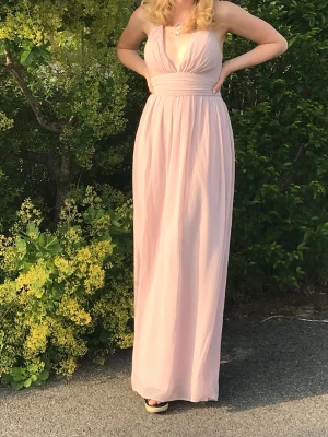 Ljusrosa långklänning/balklänning - Fin ljusrosa långklänning från NLY EVE med v-ringning, banden är korsade i ryggen och den är lite djup i ryggen. Färgerna på andra bilden är lite missvisande. Perfekt inför student/universitets balen! 