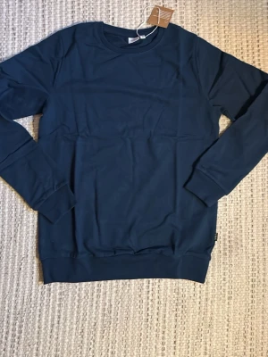 Mörkblå sweatshirt från Name It - En stilren mörkblå sweatshirt från Name It i mjuk bomull. Tröjan har rund halsringning, långa ärmar och ribbade muddar vid ärmslut och nederkant. Perfekt för en avslappnad och enkel look.