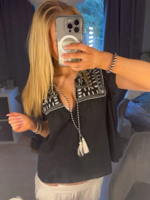 Svart Blus Med Snören - Säljer en jättefin svart blus med vita snören & detaljer. Köpt i L men är vanligtvis i str S och passar ändå bra! Kommer tyvärr inte längre till användning. Skriv för info eller bilder!🩷