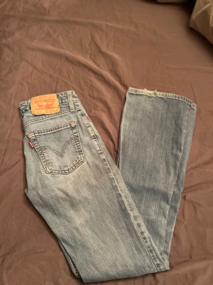 Bootcut jeans från Levis  - Säljer ett par klassiska ljusblå Levi's jeans med slitning vid knät och låg midja. Perfekta för en avslappnad och trendig look.