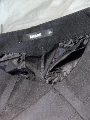 Svarta Kostymbyxor från bikbok  - Säljer ett par svarta högmidjade kostymbyxor från BikBok i storlek 34. Byxorna har en snygg, figurnära passform upptill och lite utsvängda ben.