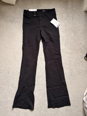 Svarta bootcut kostymbyxor Bershka - Helt nya svarta kostymbyxor från Bershka, aldrig använt då de var för små för mig i bootcut-modell. Byxorna har hög midja, två knappar framtill, dragkjedja och ficka med knapp baktill. I storlek EUR 38