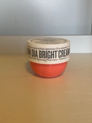 Sol de Janeiro Bom Dia Bright Cream - Bom Dia Bright Cream från Sol de Janeiro i en rund, orange plastburk med vitt lock. Innehåller AHA och vitamin C för att ge huden lyster och mjukhet. Perfekt för dig som vill boosta huden med fukt och glow. Doften är fräsch och burken är smidig att ta med.