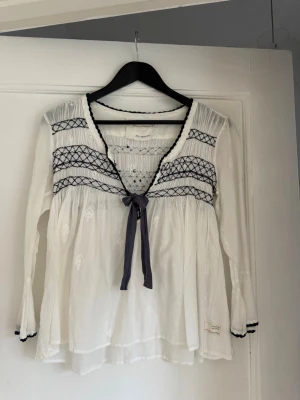 Vit Odd Molly blus med brodyr - Supersöt vit blus från Odd Molly med mörkblå brodyrdetaljer och knytband framtill. 