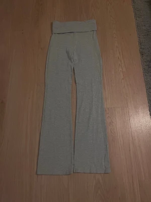 Gråa bootcut leggings med hög midja - Säljer ett par ljusgrå leggings med bootcut-ben och bred, hög midja. Tillverkade i mjukt och stretchigt material som sitter skönt på kroppen. Perfekta för en avslappnad och trendig look. Inga synliga loggor eller märken.
