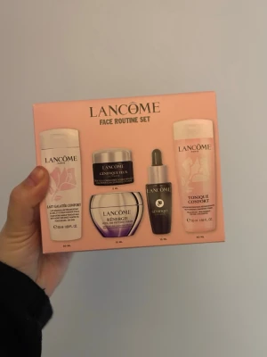 Lancôme Face Routine Set - Säljer ett Lancôme Face Routine Set med fem hudvårdsprodukter i miniformat. Setet innehåller rengöring, toner, ögonkräm, ansiktskräm och serum. Förpackningen är ljusrosa med eleganta illustrationer och produkterna har vita, svarta och lila detaljer.