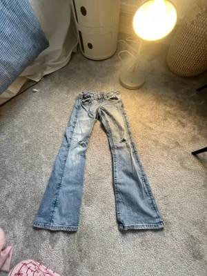 Ljusblå bootcut jeans med slitningar, ganska små i storlek. - Säljer ett par ljusblå bootcut jeans med slitningar och tvättade detaljer. Jeansen har klassisk femficksmodell, låg midja och vida ben. Perfekta för en avslappnad och trendig look. Materialet är denim i bomull.