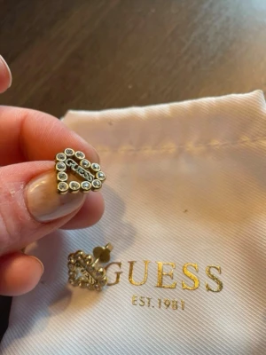 Guldiga triangelformade örhängen Guess - Säljer ett par guldiga triangelformade örhängen från Guess. Örhängena är dekorerade med små pärlliknande detaljer runt hela formen och har en snygg, modern design. Perfekta för dig som vill ha något trendigt och stilrent från ett välkänt märke.Betalning via vanlig swish!!