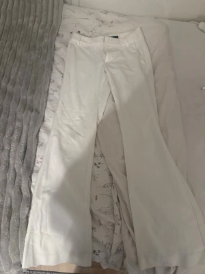 Kostymbyxor - Säljer ett par vita kostymbyxor med utsvängda ben och klassisk midja. Byxorna har hällor för skärp och stängs med dragkedja och knapp. Perfekta för en stilren och trendig look. Köpta på bikbok. 