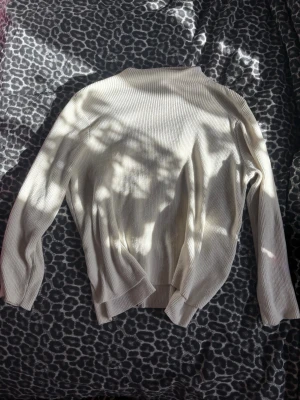 Krämvit ribbad tröja med slits - Säljer en krämvit ribbad tröja med lång ärm och snygg slitsdetalj på sidorna. Tröjan har en avslappnad passform och är tillverkad i ett mjukt, stretchigt material som känns skönt mot huden. Perfekt för dig som gillar stilrena och enkla plagg.