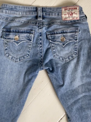Ljusblå True Religion jeans - Säljer ett par ljusblå jeans från True Religion med ikoniska bakfickor och snygga kontrastsömmar. I modellen joey. Storlek w24, säljer pga att de är för stora för mig. 💗De är nya och har använt de max 2 gånger! Jag har sytt upp de då de passar mig som är ca 158 cm. Skriv vid frågor!