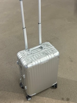 Silverfärgad kabinväska från Rimowa - PRIS KAN DISKUTERAS Snygg och stilren kabinväska från Rimowa i silverfärgad aluminium. Väskan har fyra hjul, teleskophandtag och klassisk räfflad design. Perfekt för resor när du vill ha både funktion och design. Invändigt finns smarta fack och spännband.