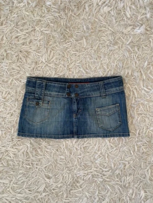 Blå jeanskjol med fickor - Säljer en kort blå jeanskjol med dubbla knappar framtill, bälteshällor och snygga fickdetaljer både fram och bak. Sååå fin och cool nu till sommaren!! Midjemått rakt över: 43cm, Längd: 25-27cm. W30 men uppskattar storleken till S/M men se mått! Jag på bilden brukar ha S-M i nederdelar och är 180 för referens☺️