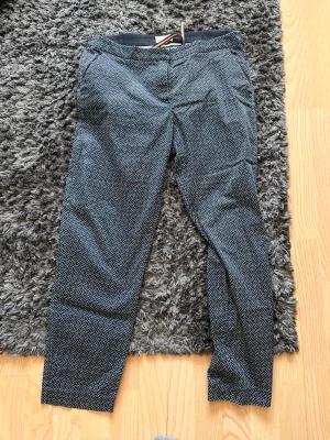 Mönstrade kostymbyxor i svart och vitt - Snygga kostymbyxor med svartvitt grafiskt mönster och smal passform. Byxorna har fickor i sidorna och bälteshällor i midjan. Perfekta för dig som vill ha en stilren men ändå unik look.