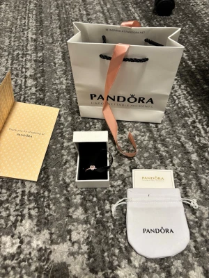 Pandora ring med hjärta och stenar - Säljer en elegant ring från Pandora i silverfärg med ett hjärtformat motiv i mitten, dekorerad med gnistrande små stenar runt hjärtat och längs ringen. Perfekt för dig som gillar romantiska detaljer och exklusiv känsla. Kommer med originalpåse och ask.