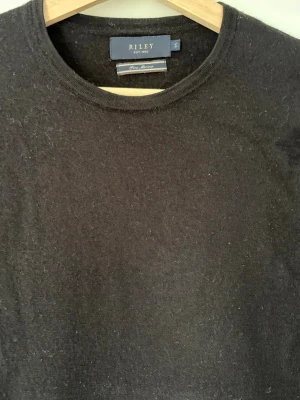 Marino ull tröja från Riley - Klassisk svart stickad tröja från Riley med rund halsringning och långa ärmar. Tröjan är tillverkad i mjukt material och har en enkel, stilren design som passar till det mesta. Perfekt för dig som gillar en clean och tidlös look. Tröjan har krympt i tvätten och passar xs 