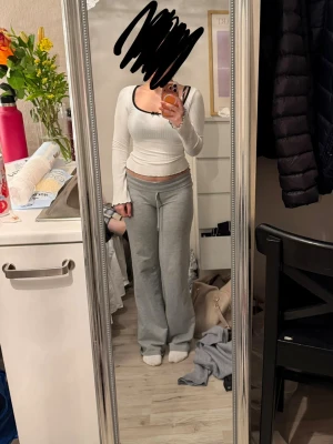 Vit ribbad långärmad topp - Säljer en vit ribbad långärmad topp med svart kant runt halsen. Toppen är croppad och har en figurnära passform som framhäver midjan. Perfekt att styla med både jeans och kjol för en trendig look.