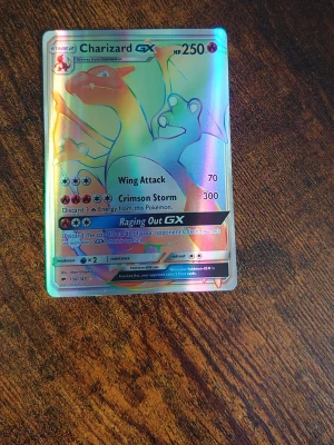 Charizard GX Pokémonkort holo - Säljer ett Charizard GX Pokémonkort med holografisk yta. Kortet har färgstarka detaljer i rött, blått och guld och visar Charizard med attacker som Wing Attack och Crimson Storm. Perfekt för samlare eller Pokémonfans.