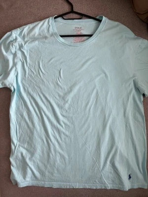 Turkos t-shirt från Polo Ralph Lauren - Säljer en turkos t-shirt från Polo Ralph Lauren i klassisk passform. T-shirten är tillverkad i 100% bomull och har korta ärmar samt den ikoniska Polo-loggan broderad i mörkblått vid nederkanten. Perfekt för dig som gillar stilrena basics.