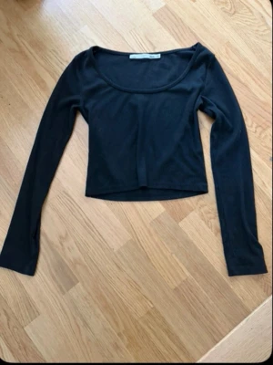 Svart långärmad croppad topp - En svart långärmad topp med croppad passform och rundad halsringning. Perfekt att styla med jeans eller kjol för en trendig look. Enkel och stilren design som passar till många outfits.