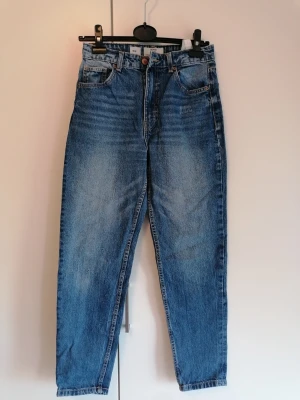 Blå mom jeans från Bershka - Ett par klassiska blå mom jeans från Bershka med hög midja och raka ben. Jeansen har fem fickor, knapp- och dragkedjegylf samt snyggt tvättad denim. Perfekta för en avslappnad och trendig stil.