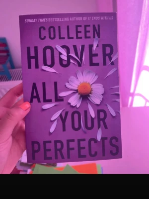 All Your Perfects av Colleen Hoover - En skönlitterär bok med lila omslag och en prästkrage som motiv. Titeln 'All Your Perfects' är tryckt i stora svarta bokstäver. Boken är i pocketformat och har en modern, stilren design. Perfekt för dig som gillar romantik och känslostarka berättelser.