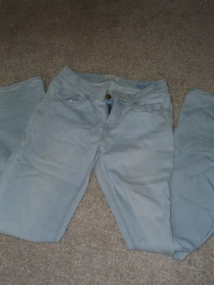 Ljusblå jeans med fler passform - Säljer ett par ljusblå jeans med klassisk femficksdesign och fler i passform. Jeansen har knapp- och dragkedjestängning samt bälteshällor. Perfekta för en avslappnad och trendig look.