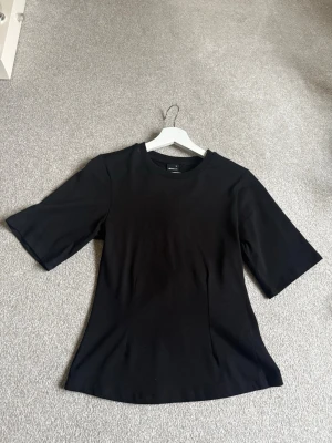 Svart t-shirt från Gina Tricot - En stilren svart t-shirt från Gina Tricot med rund halsringning och halvlånga ärmar. Tillverkad i mjukt och stretchigt material som sitter snyggt på kroppen. Perfekt basplagg att matcha med allt i garderoben.