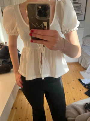 Vit blus med puffärmar och knyt - Supersöt vit blus från Gina Tricot aldrig andvänd och den har puffärmar och knyt framtill. Blusen har en djup rundringning, lätt rynkad midja och är tillverkad i ett luftigt, strukturerat tyg. 