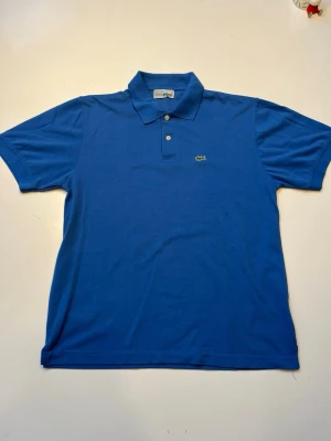 Blå pikétröja från Lacoste - Snygg blå pikétröja från Lacoste. Använd ett fåtal gånger med varsamhet.  Perfekt fynd till sommaren så du har den redo😀 skriv vi minsta funderingar så svarar jag så snabbt som möjligt. Pris kan diskuteras!