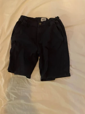 Mörkblå shorts med knapp - Snygga mörkblå shorts med klassisk passform och knapp framtill. Shortsen har resår i midjan och två sidofickor. Perfekta för varma dagar och enkla att matcha med olika toppar.