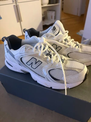 Vita New Balance sneakers - Säljer ett par vita New Balance sneakers modell 530 med mesh och syntetmaterial. Skorna har klassisk N-logga på sidan, vita snören och detaljer i mörkblått. Som nya har använt dom 2 ggr på gymmet  finns inga defekter alls  nypris 1499 ca inköpta på stsdium kvitto finns 