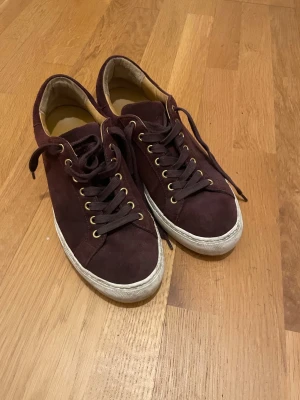 Vinröda sneakers i mocka Sneaky Steve - Snygga vinröda sneakers i mocka med vita sulor och guldfärgade öljetter. Klassisk låg modell med matchande vinröda skosnören. Perfekta för dig som vill ha en stilren och trendig look till vardags. Skorna har en enkel och tidlös design. Finns tecken på användning, FINNS INGEN LÅDA