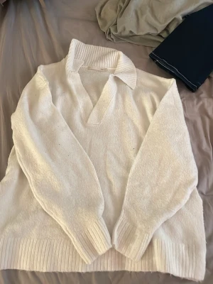 Vit stickad tröja med krage - Säljer en vit stickad tröja med bred krage och v-ringning. Tröjan har långa ärmar och ribbstickade muddar vid ärmslut och nederkant. Perfekt för lager-på-lager och en clean look.