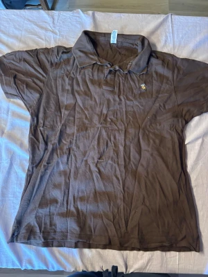 Brun pikétröja från Ralph Lauren - Klassisk brun pikétröja från Ralph Lauren med korta ärmar och krage. Tröjan har den ikoniska broderade loggan på bröstet och är tillverkad i mjuk bomull. Perfekt till jeans eller shorts för en avslappnad look. Har fått den från en kompis så är inte säker om den är äkta eller inte 