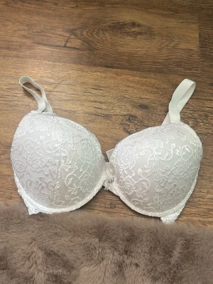 Vit spets-bh med vadderade kupor - Säljer en vit bh med vadderade kupor och vacker spets över hela framsidan. Bh:n har justerbara axelband och bygel för extra stöd. Perfekt för dig som gillar en feminin och stilren look.  Bella push up. Använd fåtal gånger storlek G70.                         Nypris: 249 